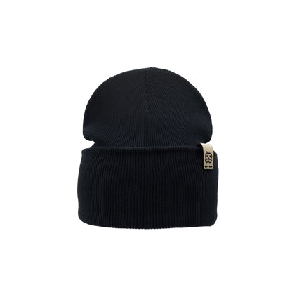 A black knit Organic Beanie by Goggleface, featuring a folded brim with a small beige tag displaying a black design. This timeless accessory is perfect for any wardrobe and is showcased against a plain white background.