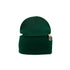 A green knit Organic Beanie from Goggleface with a folded cuff is shown. The beanie features a small rectangular fabric tag on the cuff with minimalistic branding. The texture of the knit is visible, giving it a cozy, warm appearance, making it a timeless accessory in sustainable fashion.